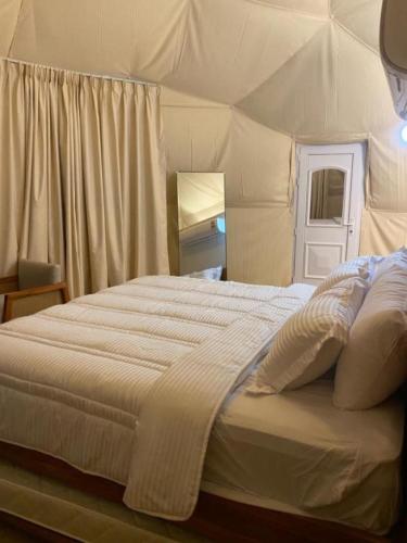 a bedroom with a large bed with white sheets at Private VIP Tent in the Desert in Ḩawīyah