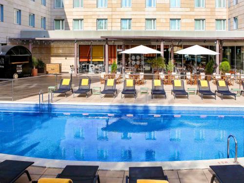 basen z krzesłami i stołami oraz budynek w obiekcie Novotel Barcelona Cornellà w mieście Cornellà de Llobregat