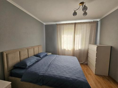 a bedroom with a bed with a blue comforter and a window at Квартира in Zhezdi