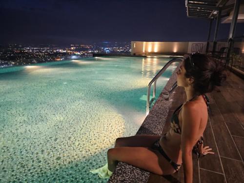 a woman sitting on the edge of a swimming pool at night at The Quartz Residence Peaceful Suites By GGM - Malacca City Centre in Melaka