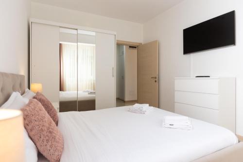 a bedroom with a white bed with a tv on the wall at Touch and Go Apartment near Bucharest Airport in Otopeni