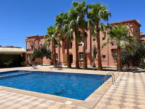 une piscine devant un immeuble avec des palmiers dans l'établissement COMPLEXE TOURISTIQUE ARTIZANAL bab sahara, à Oulad Akkou