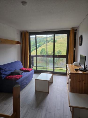 a living room with a blue couch and a large window at Studio 4pers vue piste in Le Corbier