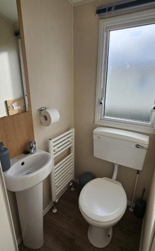 a bathroom with a toilet and a sink and a window at South Breeze Caravans in Camber