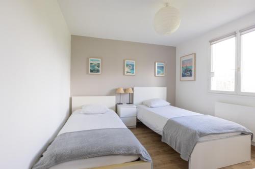 two beds in a bedroom with white walls and windows at Maison Carn Portsall in Ploudalmézeau