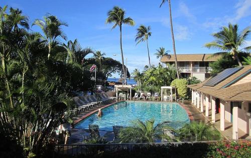a swimming pool in a resort with chairs and palm trees at Kihei Beach Condo, Romantic Kamaole II in Kihei