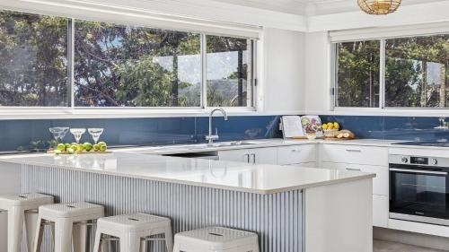 a kitchen with white cabinets and a counter with stools at Pandanus - Spacious Waterfront Escape - Holiday Yamba in Yamba