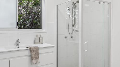 a white bathroom with a shower and a sink at Pandanus - Spacious Waterfront Escape with Private Pontoon & Pool - Holiday Yamba in Yamba