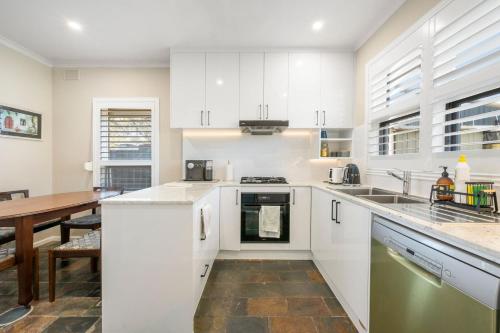 Glenungaにある4BR Home in Fullartonの白いキャビネットと木製のテーブルのあるキッチン