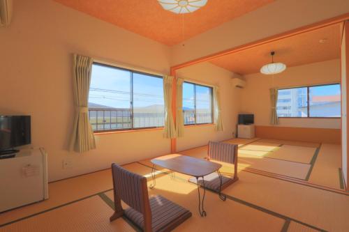 Una sala de estar con mesa y sillas y ventanas. en Travel Inn Ikuta, en Minabe