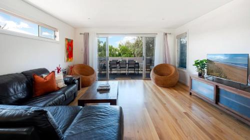 a living room with a black leather couch and a television at The Art House in Culburra Beach