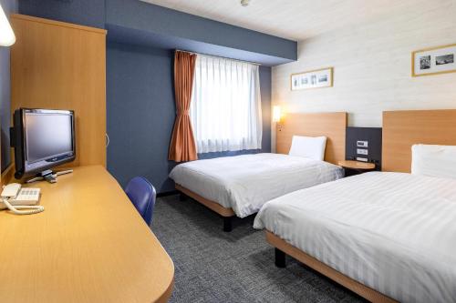 a hotel room with two beds and a desk with a tv at Comfort Hotel Niigata in Niigata