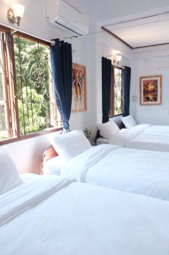 a row of white beds in a room with windows at Sabaydee Guesthouse in Ban Houayxay