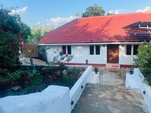 a small white house with a red roof at Emnic Cottage Homestay in Meppādi