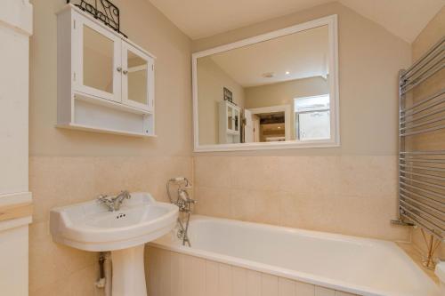 a bathroom with a sink and a tub and a mirror at Charming Cotswold Cottage on Church Green, Witney in Witney