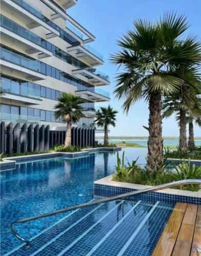 a swimming pool with palm trees in front of a building at Sunny Bliss at Yas Island - Private Beach Access in Abu Dhabi