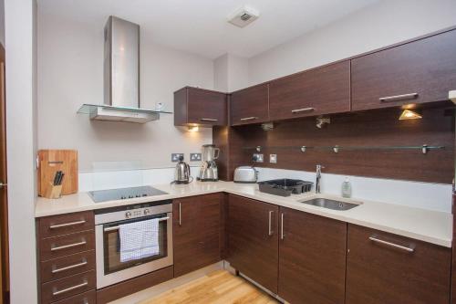 a kitchen with wooden cabinets and stainless steel appliances at Stylish Merchant City Flat Glasgow in Glasgow
