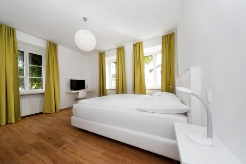 ein weißes Schlafzimmer mit einem großen weißen Bett und Fenstern in der Unterkunft Amedeo Zotti Residence Salzburg in Salzburg