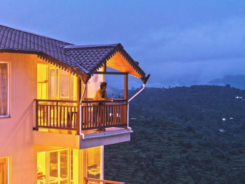 a man standing on a balcony of a building at SaffronStays Ridgeview Manor, Mukteshwar - 3BHK Villa with Himalayan Views & Verandahs in Mukteshwar