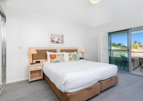 Un dormitorio con una cama grande y un balcón. en Pacific Blue Poolside Escape, en Salamander Bay