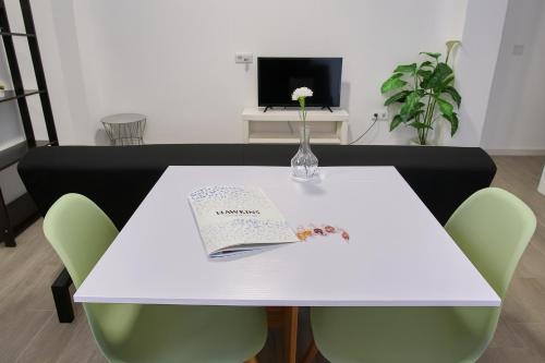 a white table with green chairs and a vase with a book at Suite by Hawkins interior 2A in Algeciras