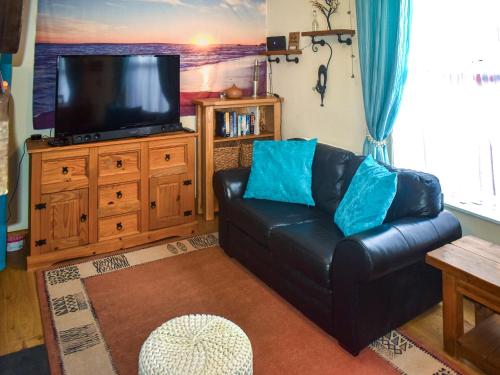 a living room with a black leather couch and a flat screen tv at Mariners Cottage in Dawlish