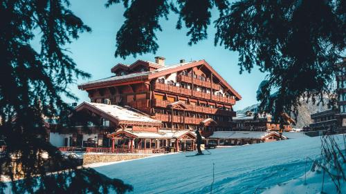 a large wooden building in the snow with a skier in front at Hotel Le Carlina Courchevel 1850 in Courchevel