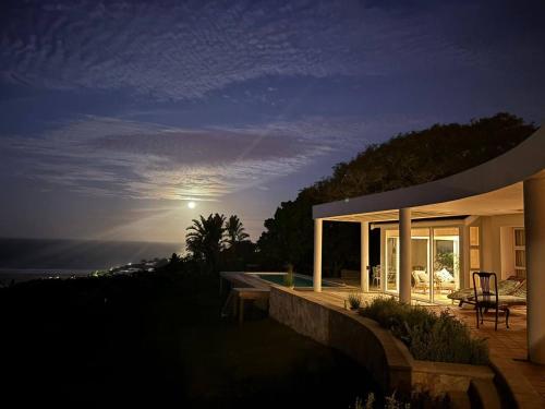 a house with a view of the ocean at night at Moon Tide Villa - 5BD w Pool & Panoramic Sea Views in Plettenberg Bay