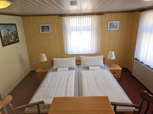 two beds in a room with two tables and two windows at Gasthaus Wolfsschlucht in Herzberg
