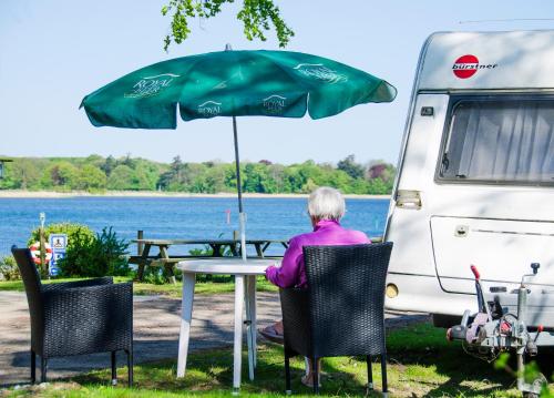 a woman sitting at a table under an umbrella next to a van at Nysted Strand Camping & Cottages in Nysted