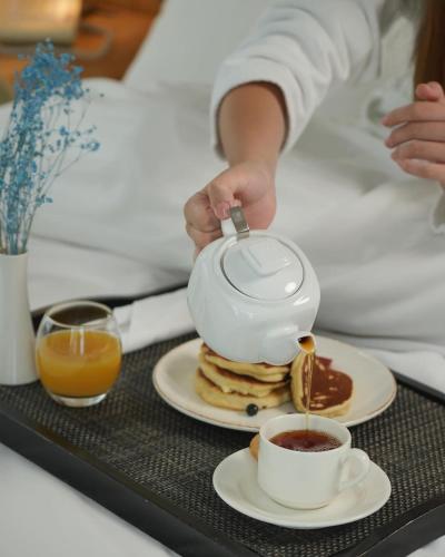 a person pouring a tea pot on a stack of pancakes at ORBI CITY - ELIT LUXURY hotel in Batumi