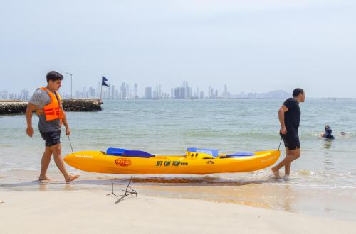 Deux hommes marchent sur la plage avec un kayak jaune dans l'établissement Casa de playa Kommox Beach, à Carthagène des Indes