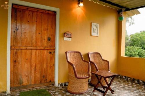 two chairs and a table on a porch with a door at Ranthambhore Bagh Dwar Camp in Khilchipur