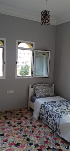 a bedroom with a bed and two windows and a rug at Appartement azla plage in Oulad Akkou