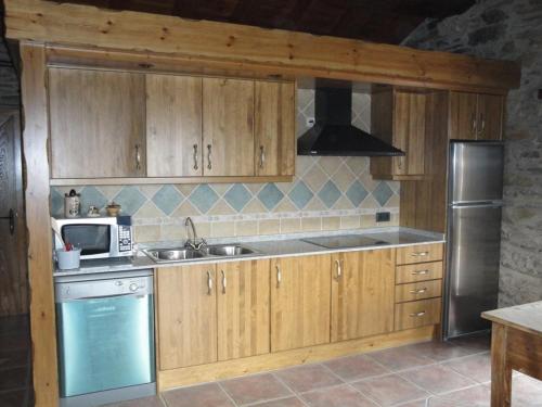 a kitchen with wooden cabinets and a sink and a microwave at La Cabanya de Cal Forn de Serrat in Queralbs