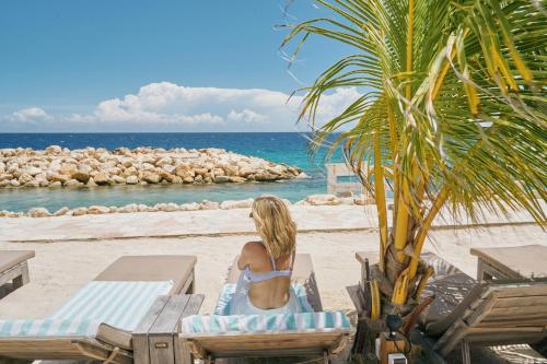 a woman in a bikini sitting on a beach at Scuba Lodge City Beach in Willemstad