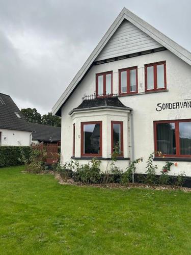 a white house with red windows and a green yard at Motel Villa Søndervang 3 personers værelse in Harndrup