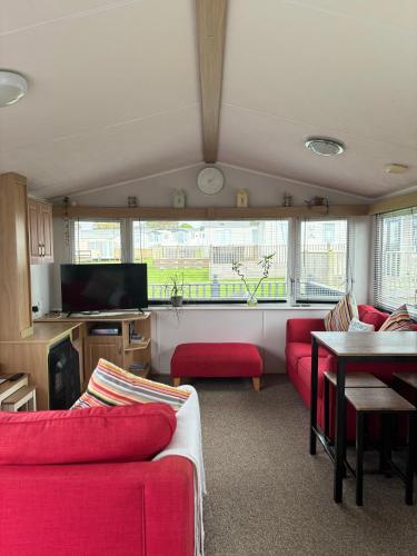 a living room with red couches and a tv at Family-Friendly 3-Bed Caravan Recently Renovated on Seven Bays Holiday Park, Padstow in Saint Merryn