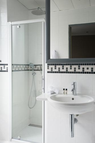 une salle de bain blanche avec un lavabo et un miroir dans l'établissement Apollon Montparnasse, à Paris