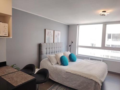 a bedroom with a bed with blue pillows and a window at Depto Estudio Full equipado con Estacionamiento in Concepción