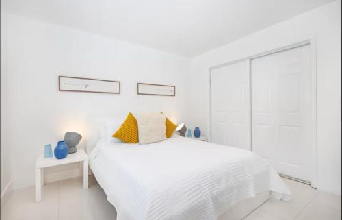 a white bedroom with a white bed with yellow pillows at GroveO6 10 minutes from the Beach in Miami