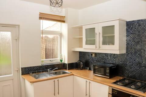 a kitchen with white cabinets and a sink and a microwave at Entire 3 Bedroom Home Rotherham in Rawmarsh