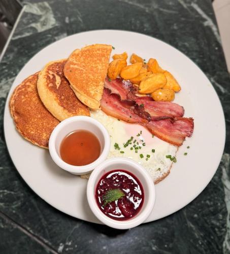 a plate of breakfast food with bacon and pancakes and dips at Hotel Prince Plaza - Laureles Estadio in Medellín