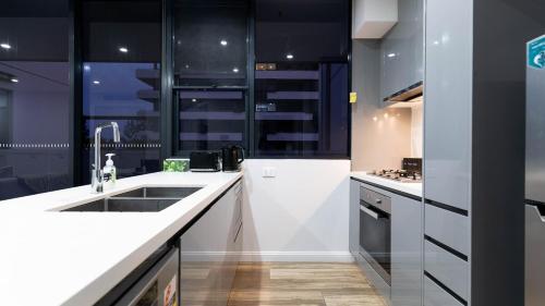 une cuisine avec des armoires noires et blanches et un évier dans l'établissement Luxe Sydney Olympic Park Stay - 2BR for 4 Guest, à Sydney