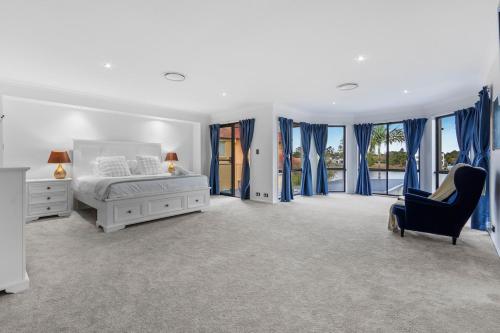 ゴールドコーストにあるSerene 5BR Waterfront Escape - Prestigeの青いカーテンとベッドと椅子のある白い寝室