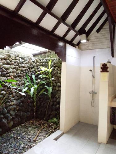 a bathroom with a stone wall and a shower at The Chapel Alam Sari Ubud in Ubud