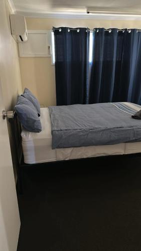 a bed in a room with a blue curtain at Quiet, Charming 3BR in Moranbah