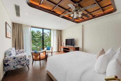 a bedroom with a white bed and a couch and a tv at Best Western Premier Sonasea Phu Quoc in Phu Quoc