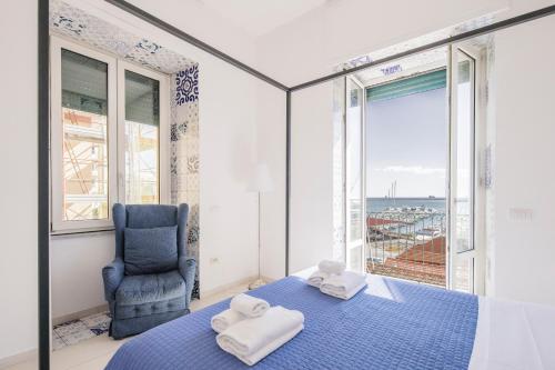 1 dormitorio con cama azul, silla y ventana en Relais Luxury Retreat - Seafront Apartments, en Salerno
