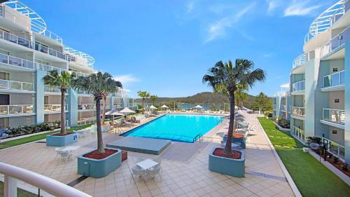 an apartment patio with a swimming pool and palm trees at Vista Mare - Beachside Studio With Stunning Views in Ettalong Beach